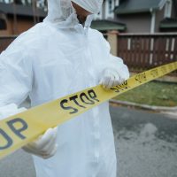 A person wearing a protective suit, handling yellow tape with 'STOP' in an outdoor urban setting.