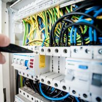 Electrical Services Hand of electrician working on a circuit breaker panel with colorful wires, ensuring safe electrical connections.