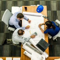 Design, Engineering & Project Management Top view of a team working on construction plans in an office setting.
