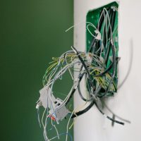 Electrical Services Opened power socket with various wires on white wall during repair at home