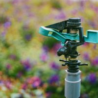 Detailed close-up of a garden sprinkler with colorful flowers in soft focus background.