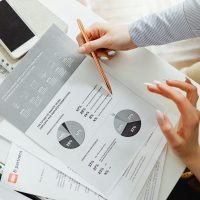 Design, Engineering & Project Management Close-up of businesswoman analyzing financial reports using pie charts in an office setting.