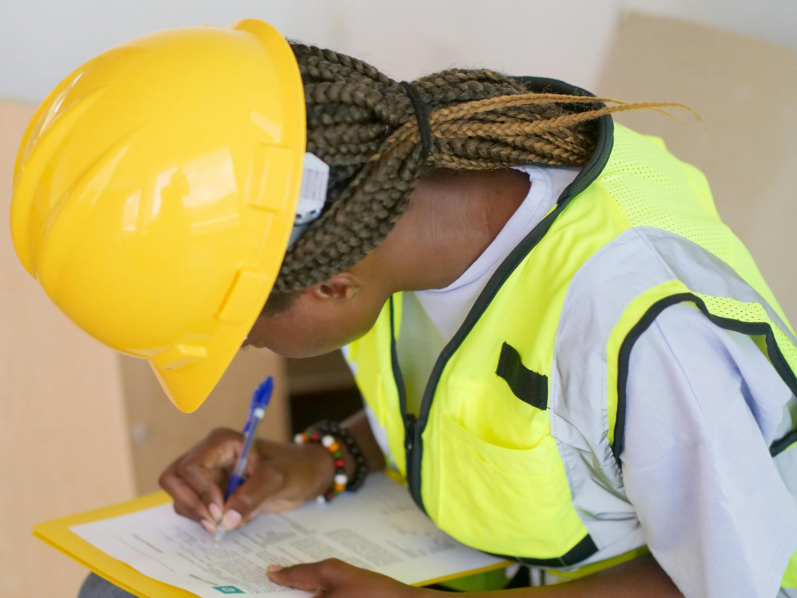 A female engineer in PPE writing on a clipboard at a construction site.